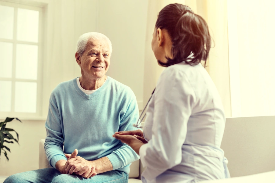 An elderly man smiles while talking to his doctor during a consultation about signs it may be time to consider palliative care.